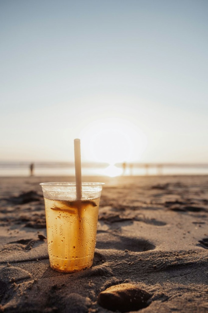 Iced cocktail in a plastic cup on the sand at sunset.