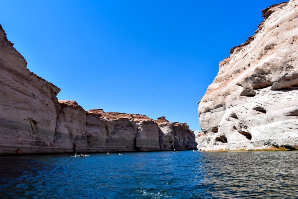 Kayakers exploring the narrow sandstone canyons and clear blue waters of Lake Powell under a bright desert sky