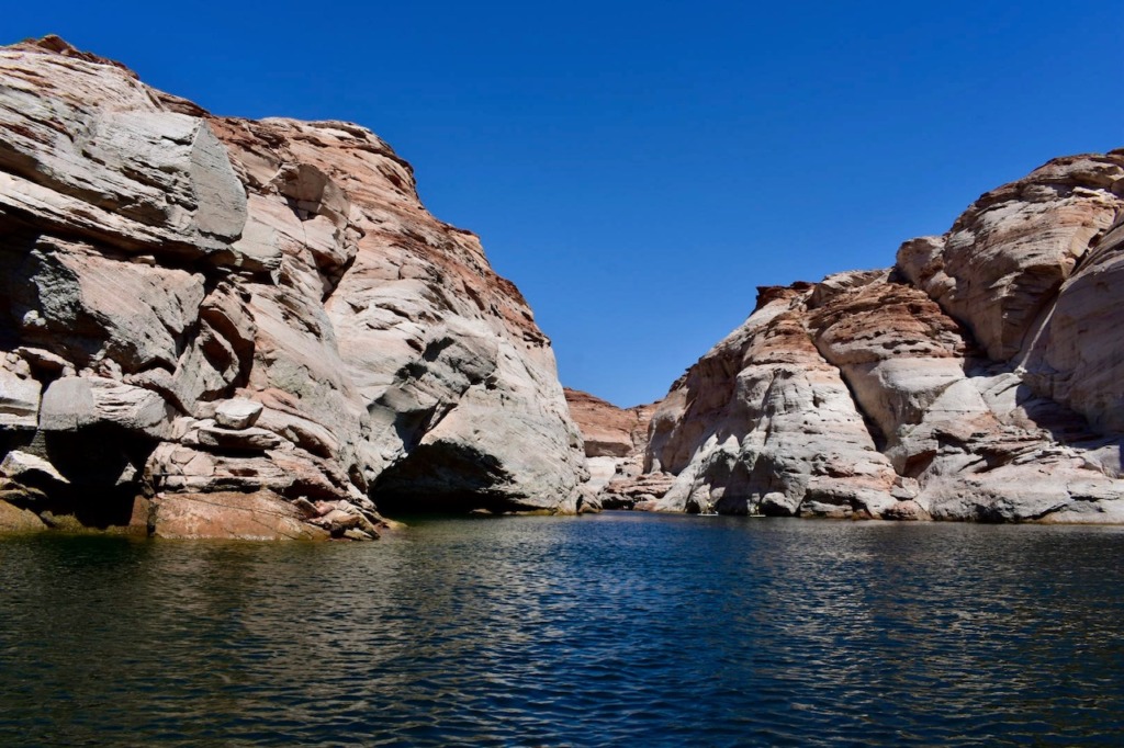 Towering red and white rock formations surrounding the calm waters of Lake Powell on a sunny day