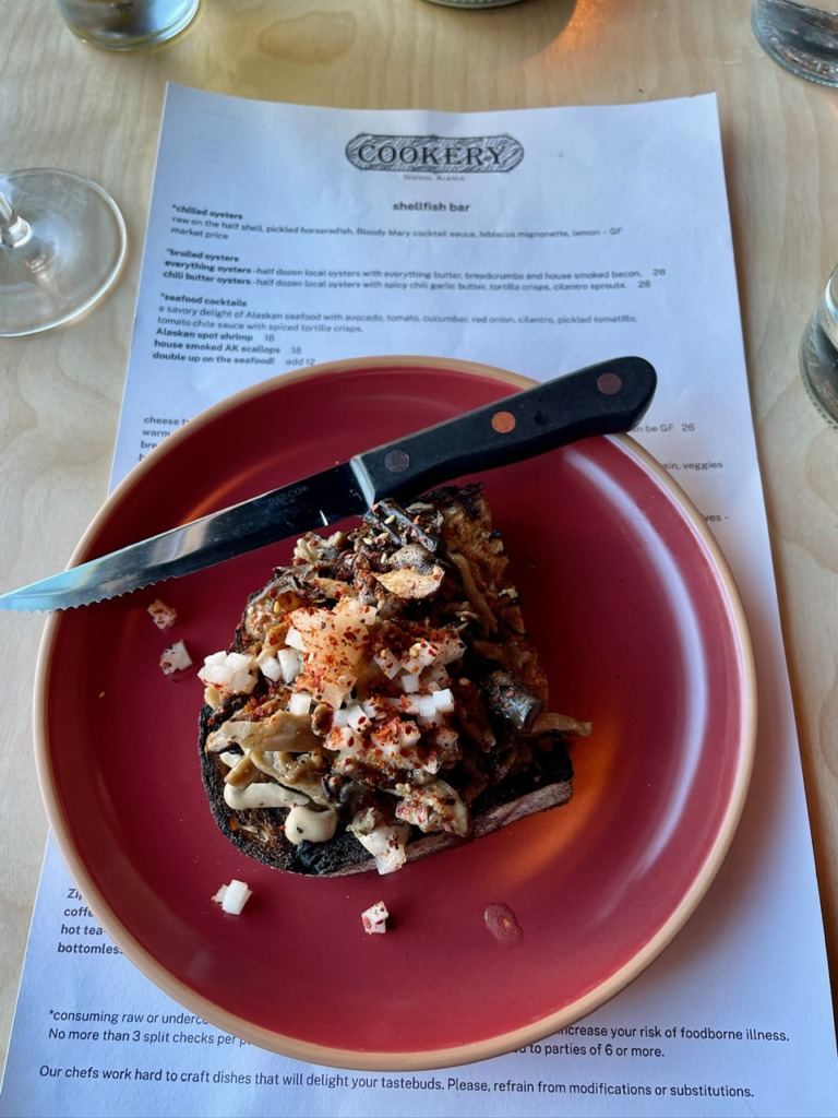 Mushroom toast with herbs and cheese served at The Cookery restaurant in Seward, Alaska, with menu in background.