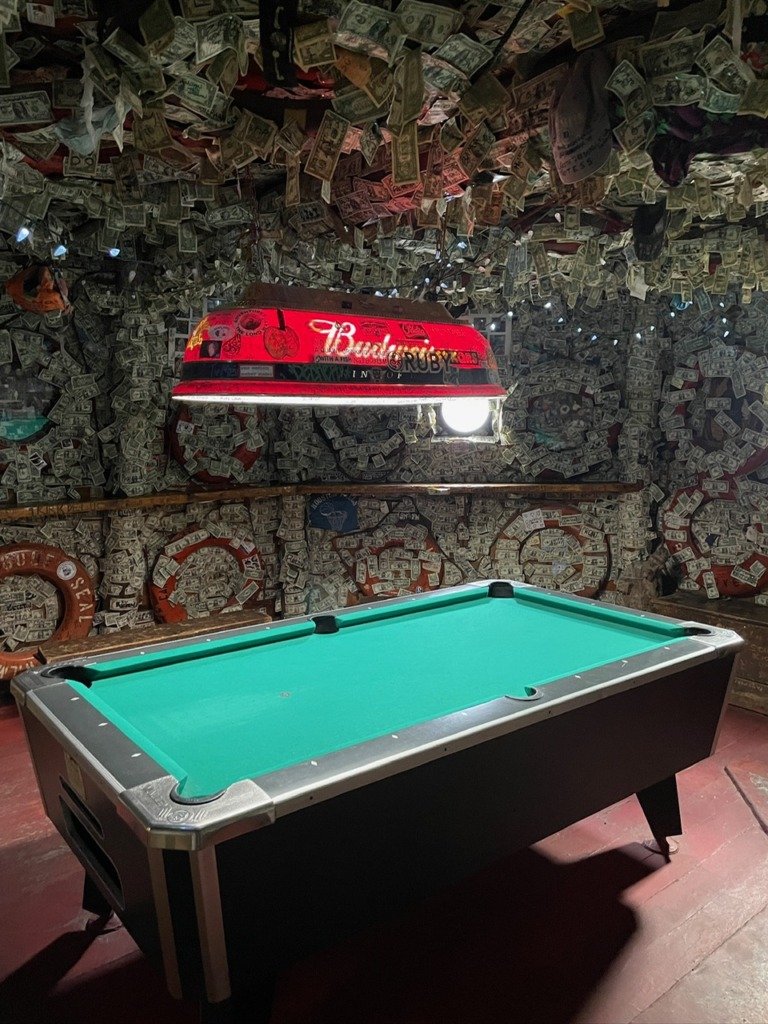 Pool table inside the Yukon Bar in Seward, Alaska, with walls and ceiling covered in signed dollar bills