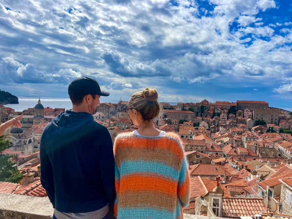 Couple looking out over the red-roofed Old Town of Dubrovnik, Croatia, from the city walls on a summer vacation, with the Adriatic Sea and dramatic cloudy sky in the background