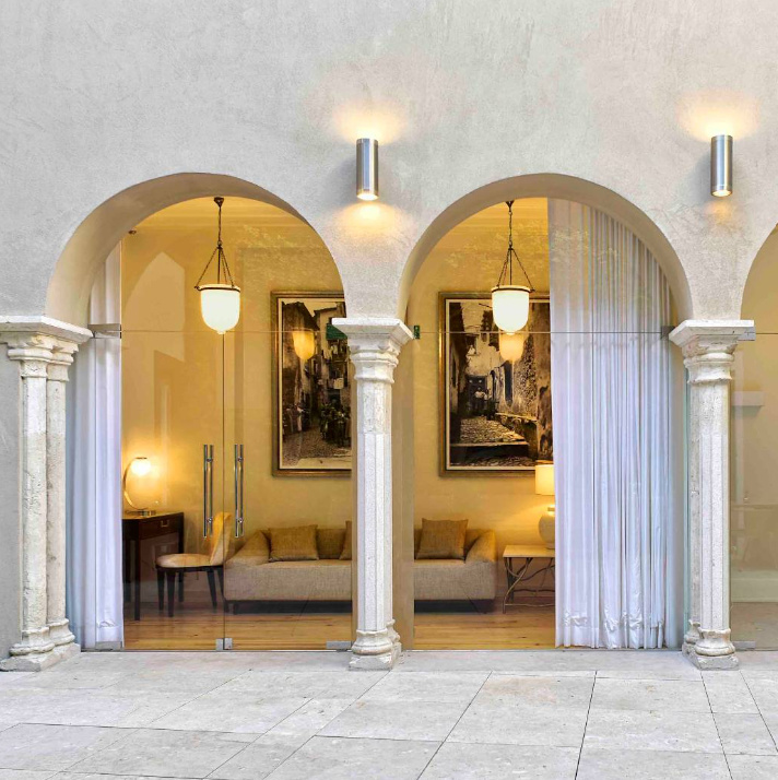 A stone-arched terrace at Santiago de Alfama hotel in Lisbon, opening onto a suite with sheer white curtains, framed black-and-white photography, and a sitting area