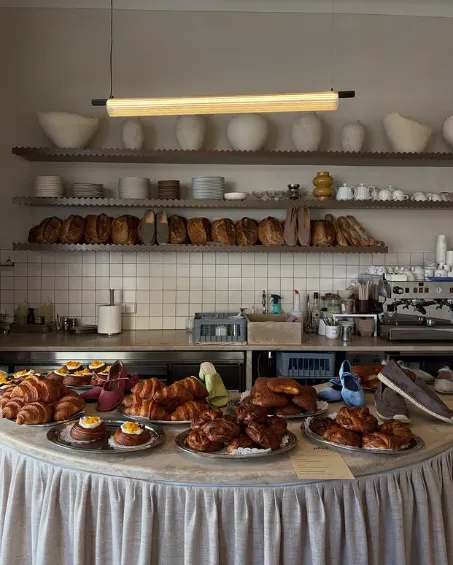 The bakery display case at Etma in Lisbon, filled with golden croissants, sourdough pastries, and tarts arranged on a counter with a linen skir