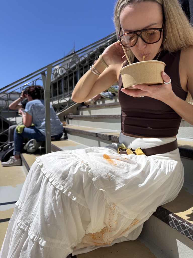 Me eating fresh pasta on the steps at Mercado do Bolhão in Porto, Portugal, with a noticeable sauce stain on my white skirt