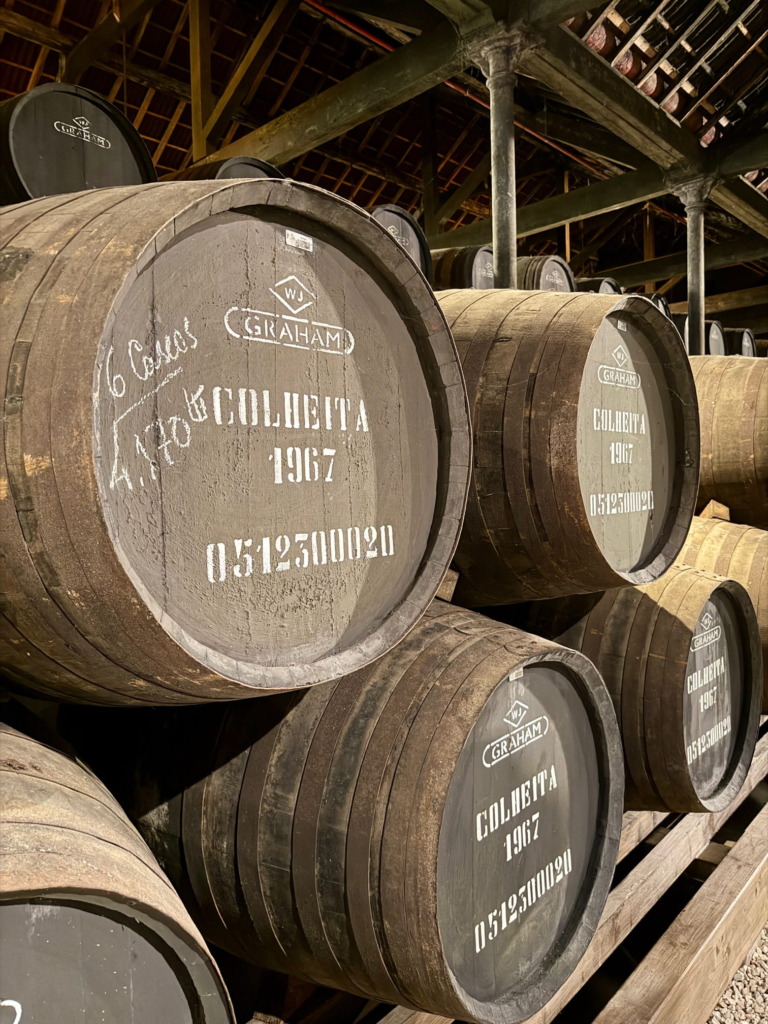 Rows of aged wooden port wine barrels stamped Graham's Colheita 1967 stacked in the dim cellar at Graham's port house in Vila Nova de Gaia, Porto