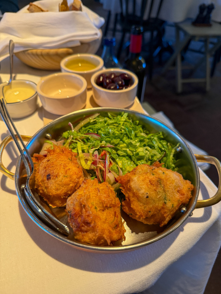 Golden fried cod cakes with shredded salad, served alongside a ramekin of estate olive oil and a bowl of olives — the dish to order first at São Lourenço do Barrocal