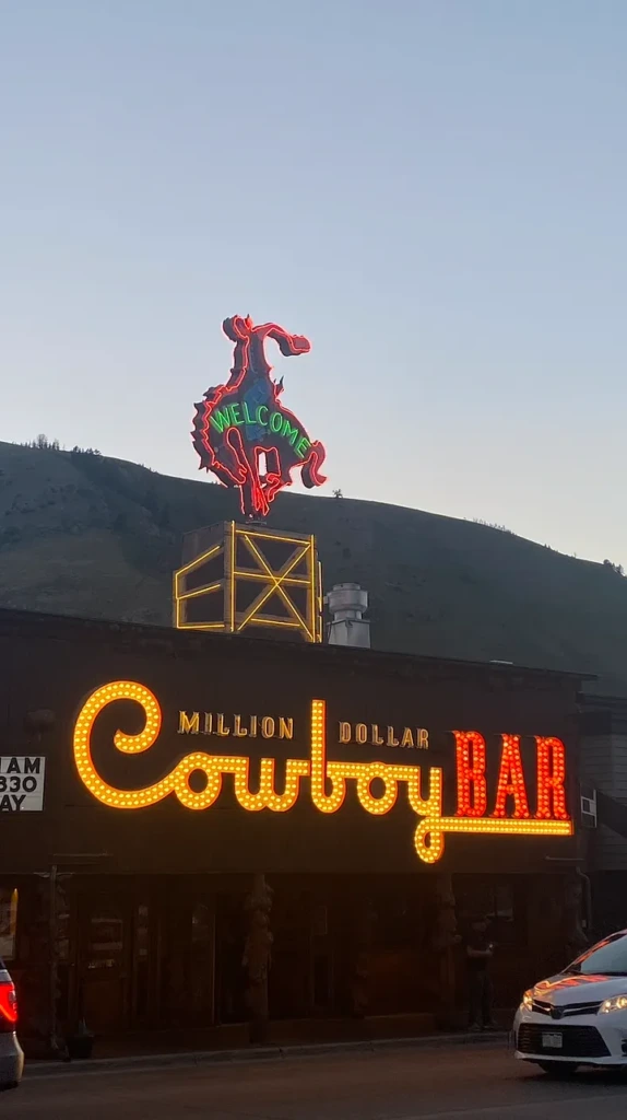 The neon 'Million Dollar Cowboy Bar' sign glowing at dusk in downtown Jackson Hole, Wyoming, with a bucking bronco sculpture on the rooftop