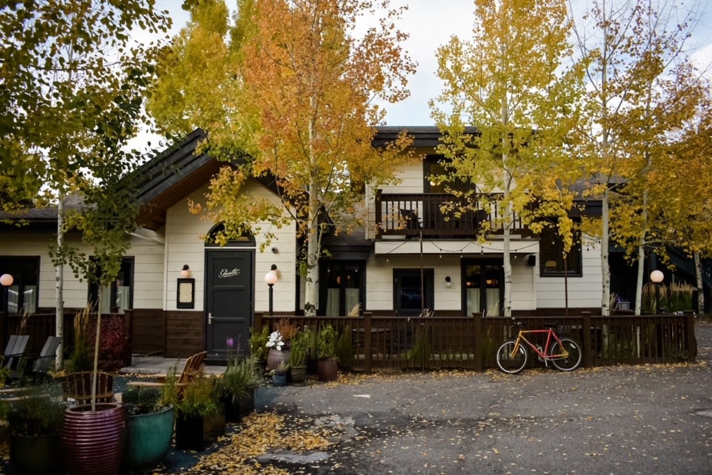 The exterior of Glorietta restaurant in Jackson Hole, Wyoming, framed by golden aspen trees in full fall color with string lights and a bicycle parked out front