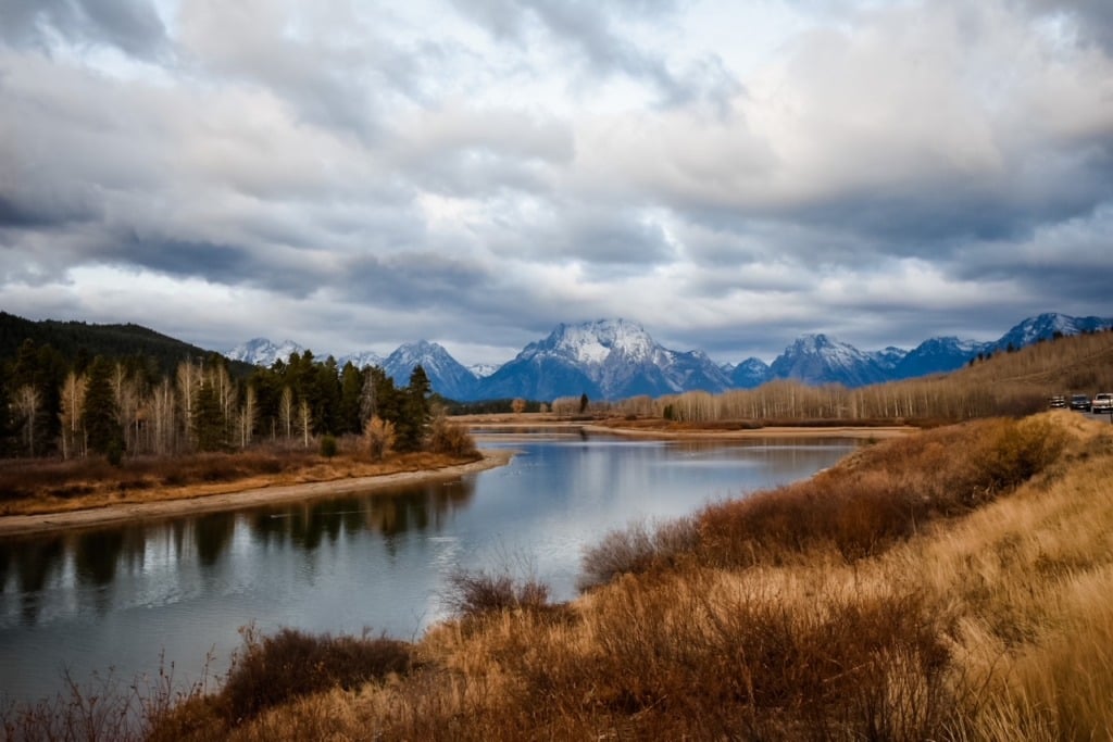 The Snake River winding through autumn brush at Oxbow Bend in Grand Teton National Park, with snow-dusted peaks reflected in the still water