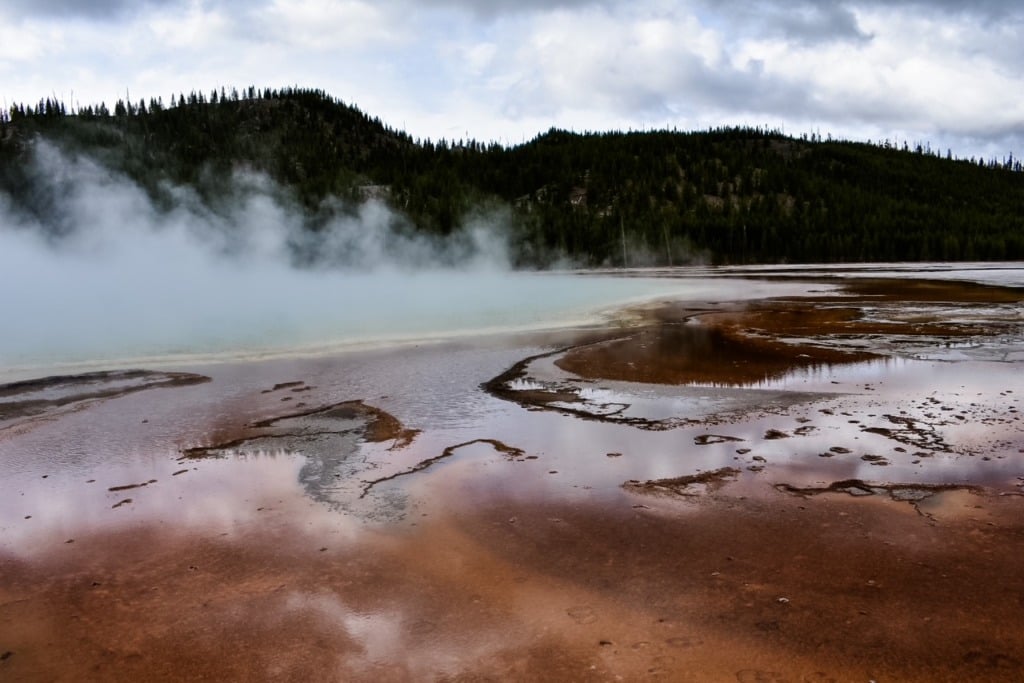 Steam rising from the vivid teal and rust-colored mineral edges of Grand Prismatic Spring in Yellowstone National Park