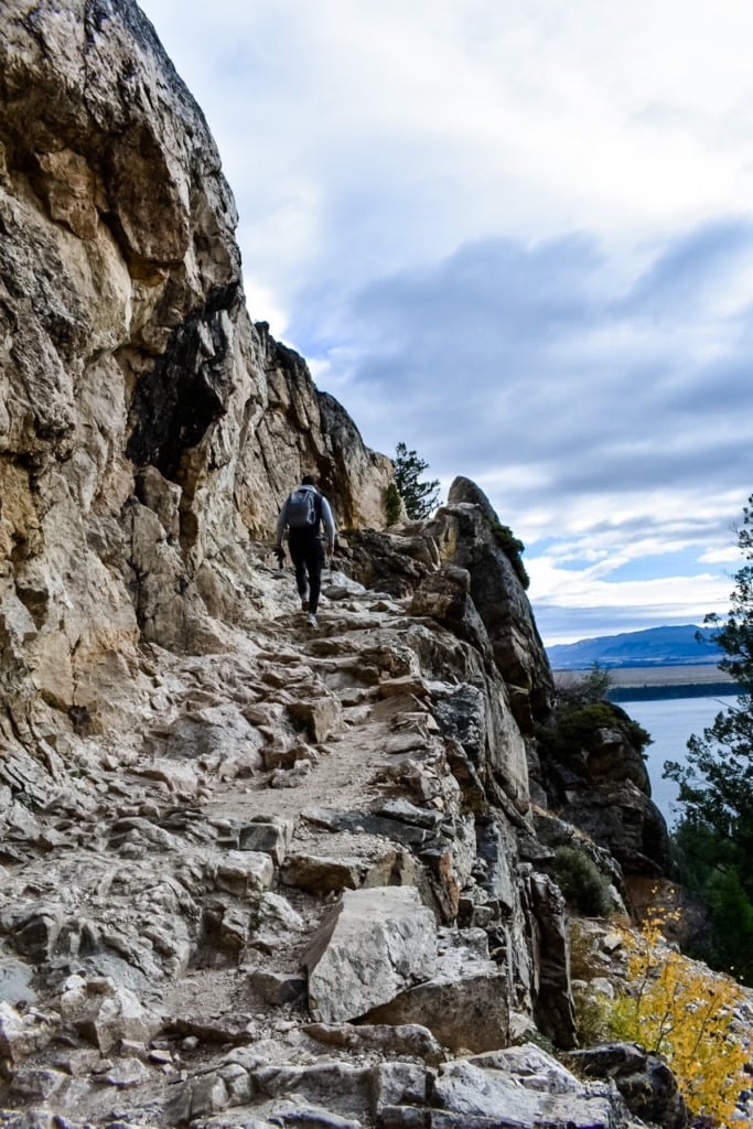 A hiker climbing a steep rocky trail above Jackson Lake on the way to Inspiration Point in Grand Teton National Park, Wyoming