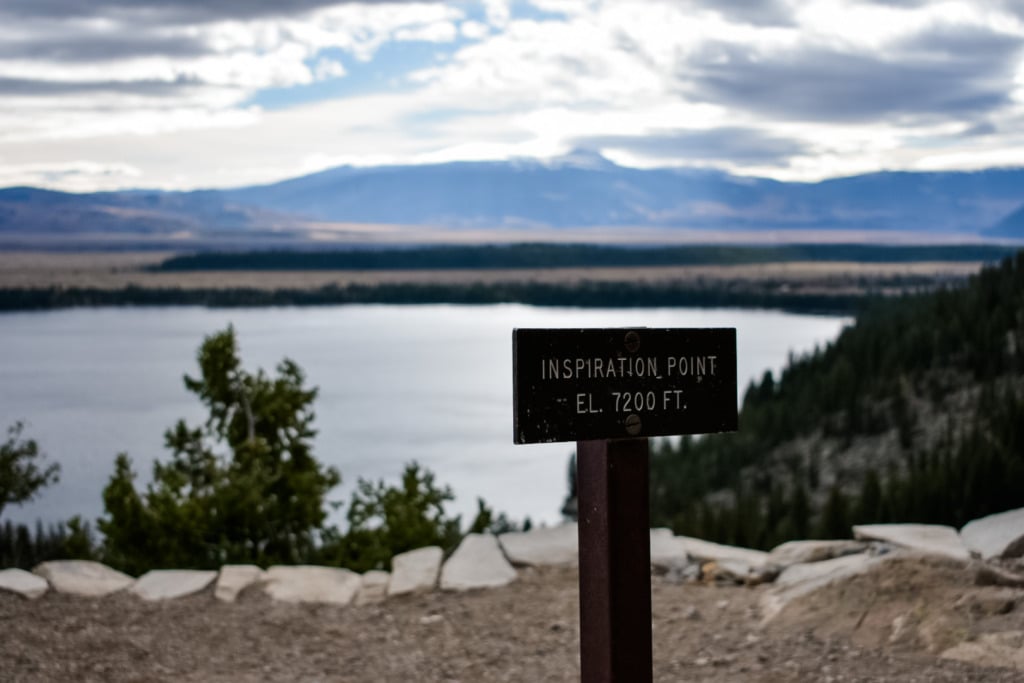 The Inspiration Point summit marker at 7,200 feet elevation in Grand Teton National Park, with Jackson Lake and the Wyoming mountain range visible below