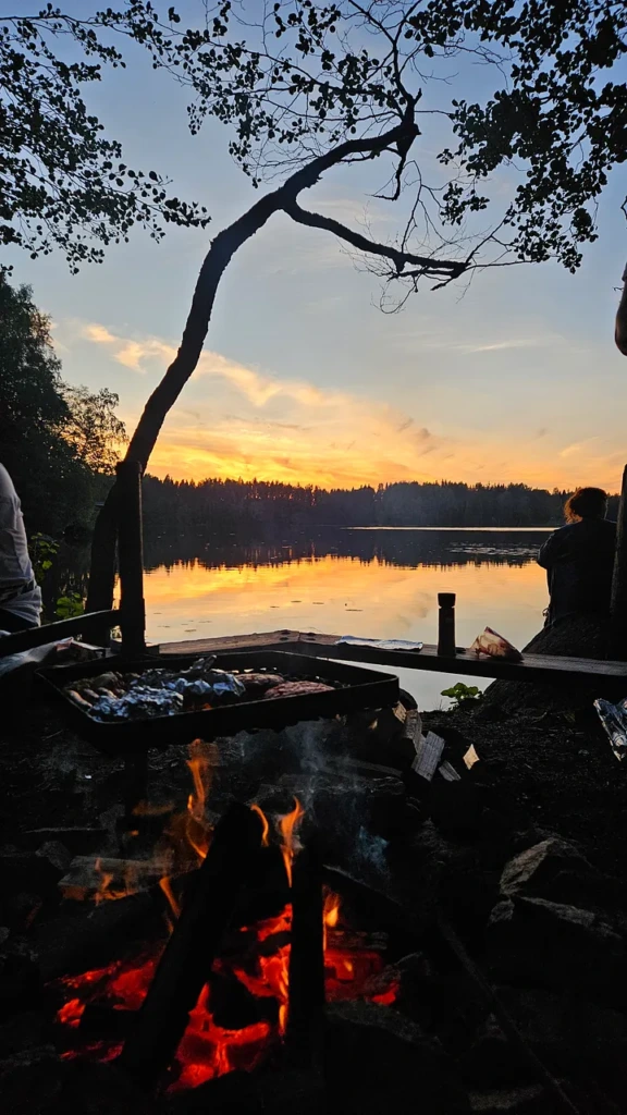 A campfire with fish grilling on a rack at the edge of Lake Winnipesaukee in New Hampshire, with a golden sunset reflected across the still water